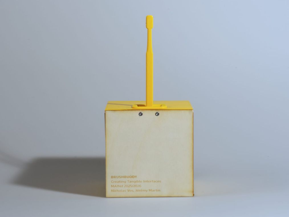 The plywood side of the cube, laser-etched with the BrushBuddy name and course credit, the brush docked on top.