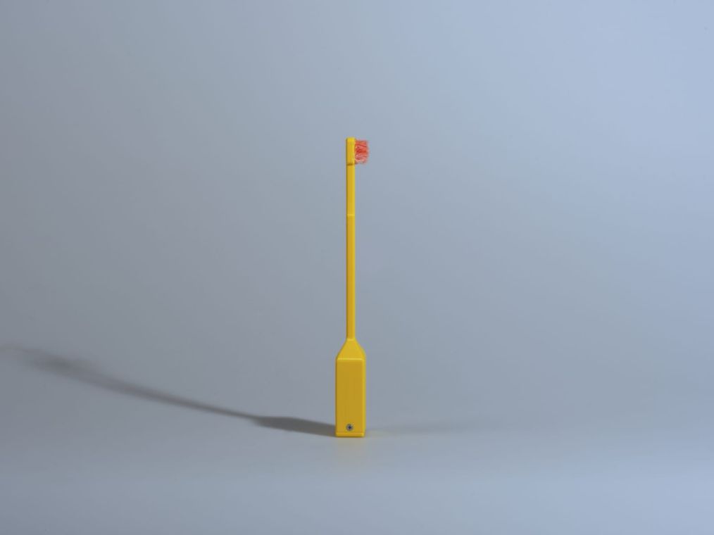The 3D-printed yellow toothbrush standing alone with red bristles at the tip, the only part of the system that moves.
