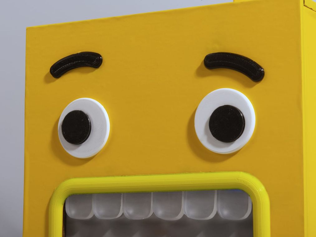 Close-up of the monster face: two raised printed eyebrows and white-and-black googly eyes above the yellow mouth frame.