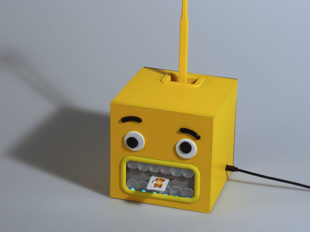 The cube powered on, a row of small blue lights along the lower teeth and a sticker dispensed into the mouth.
