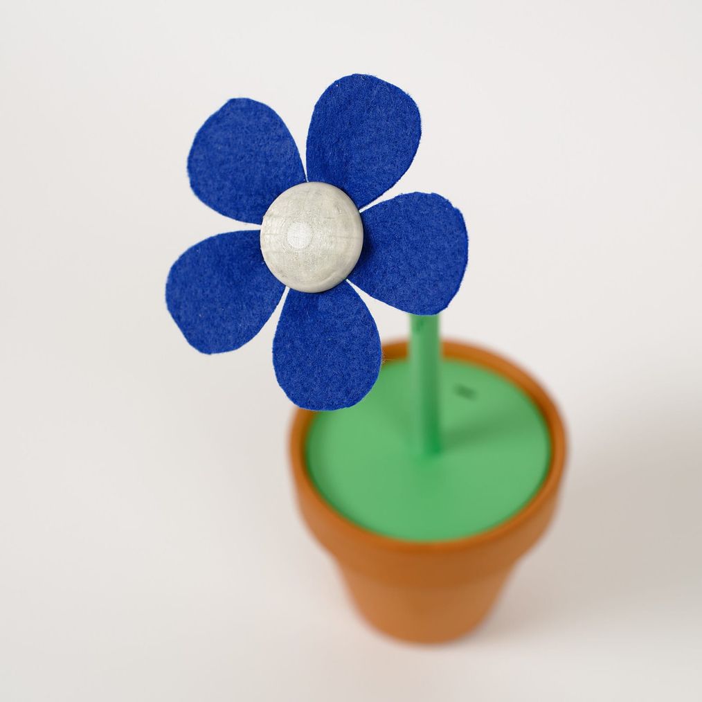 Looking down into the flower: cobalt felt petals around a pale 3D-printed center, the green stem entering the pot.