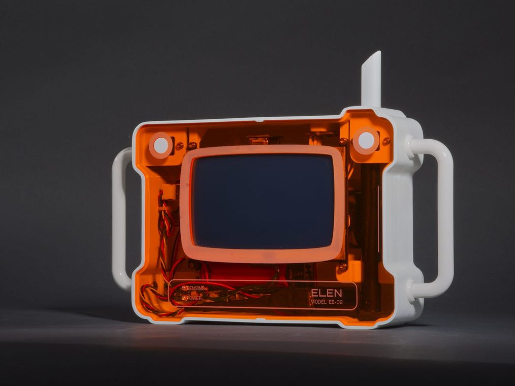 ELEN at a three-quarter angle on a gray backdrop: translucent orange body, white frame and twin handles, antenna, and the deep-blue screen.