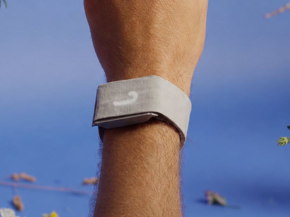 The Thea band worn on a wrist, centered in the frame, against a cobalt sky scattered with wildflowers.