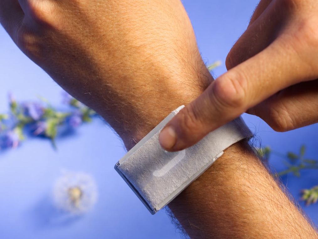 A finger pressing the device worn on the wrist, its oblong gauge lit and fine colored wires visible, against a cobalt sky.
