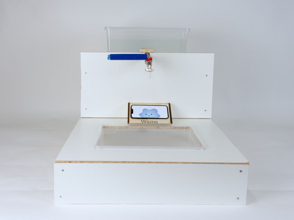 The full Wama sink rig seen head-on, tap closed, the phone in its laser-cut holder showing a smiling blue cloud.