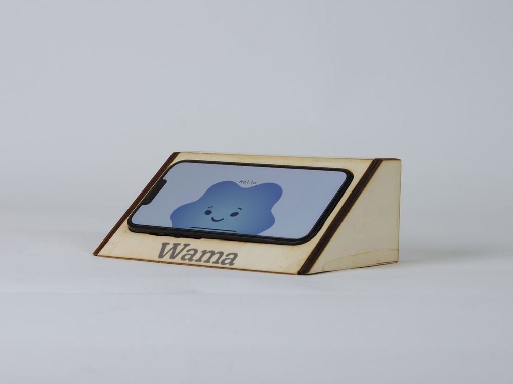 Close-up of the finger-jointed plywood holder engraved Wama, the phone showing the blue cloud greeting.