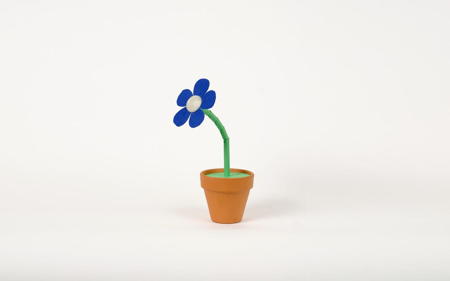 The DataBloom flower: ultramarine felt petals on a green segmented stem in a small terracotta pot, on a white studio backdrop.