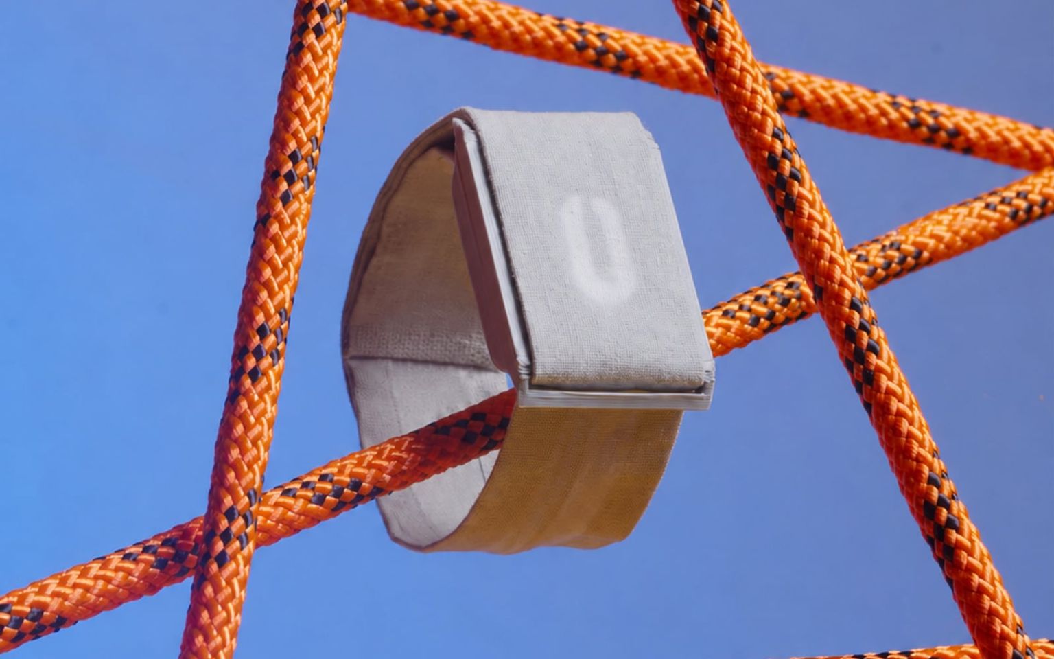 The Thea wearable suspended in a lattice of orange cords against a cobalt sky, its oblong gauge glowing, an editorial shot from the final presentation.