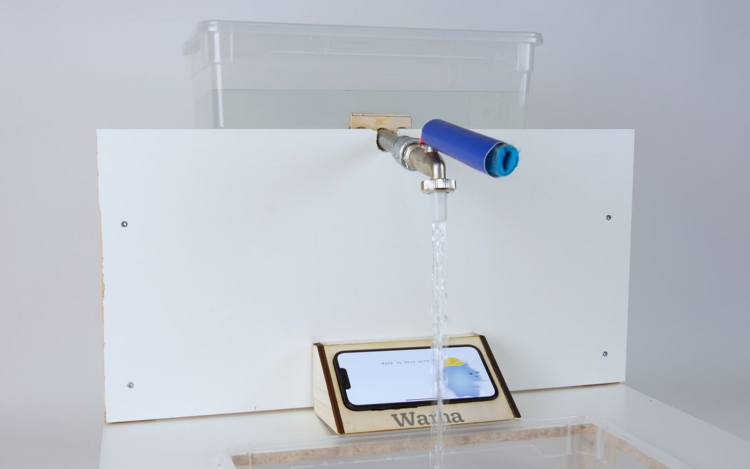 Wama's built sink rig at an angle: a tap pouring into a clear basin, the phone in its laser-cut holder showing the character.