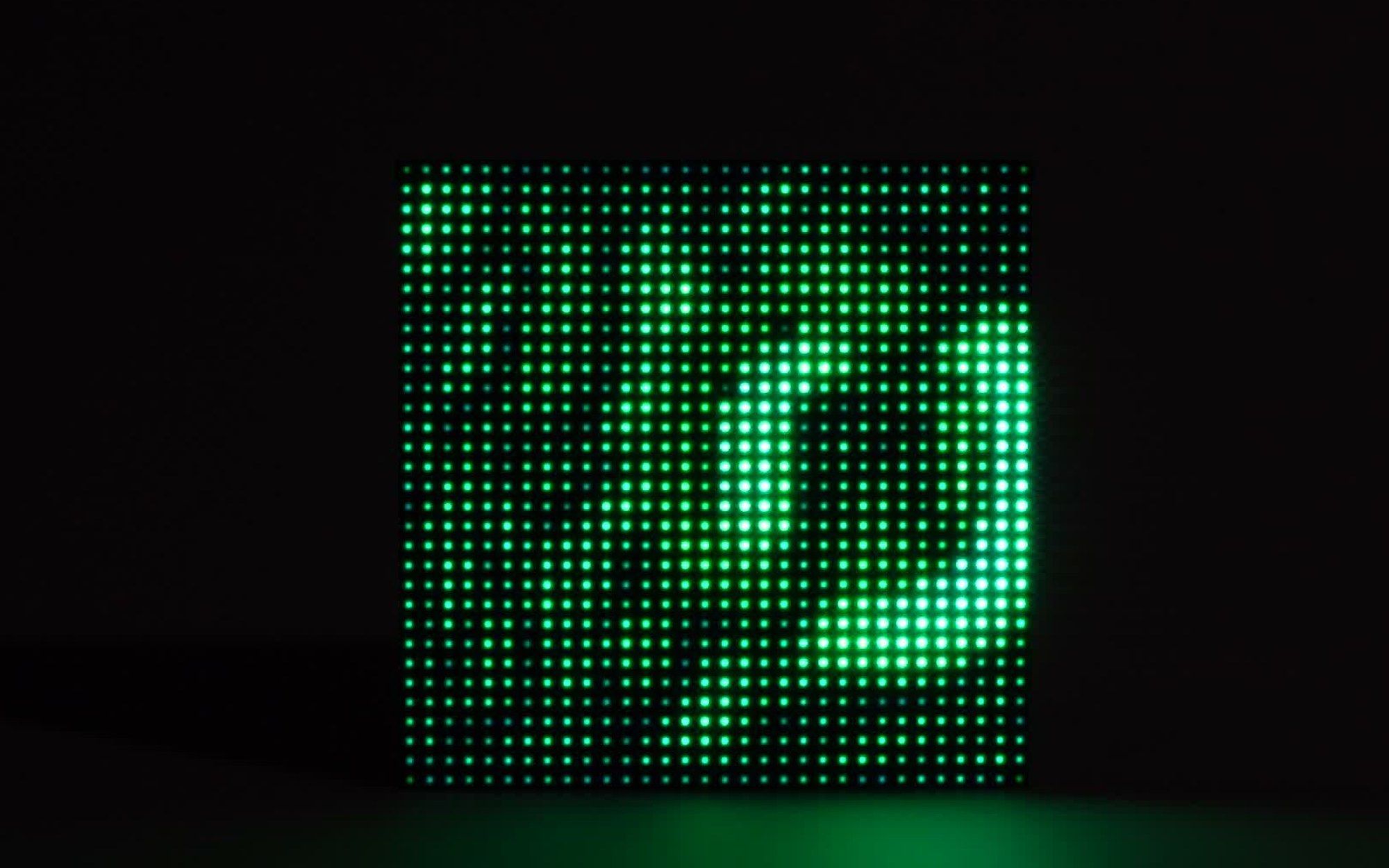 A single 32×32 LED matrix filling the frame in a dark room, green light forming a soft disturbance across the grid with every pixel distinct.