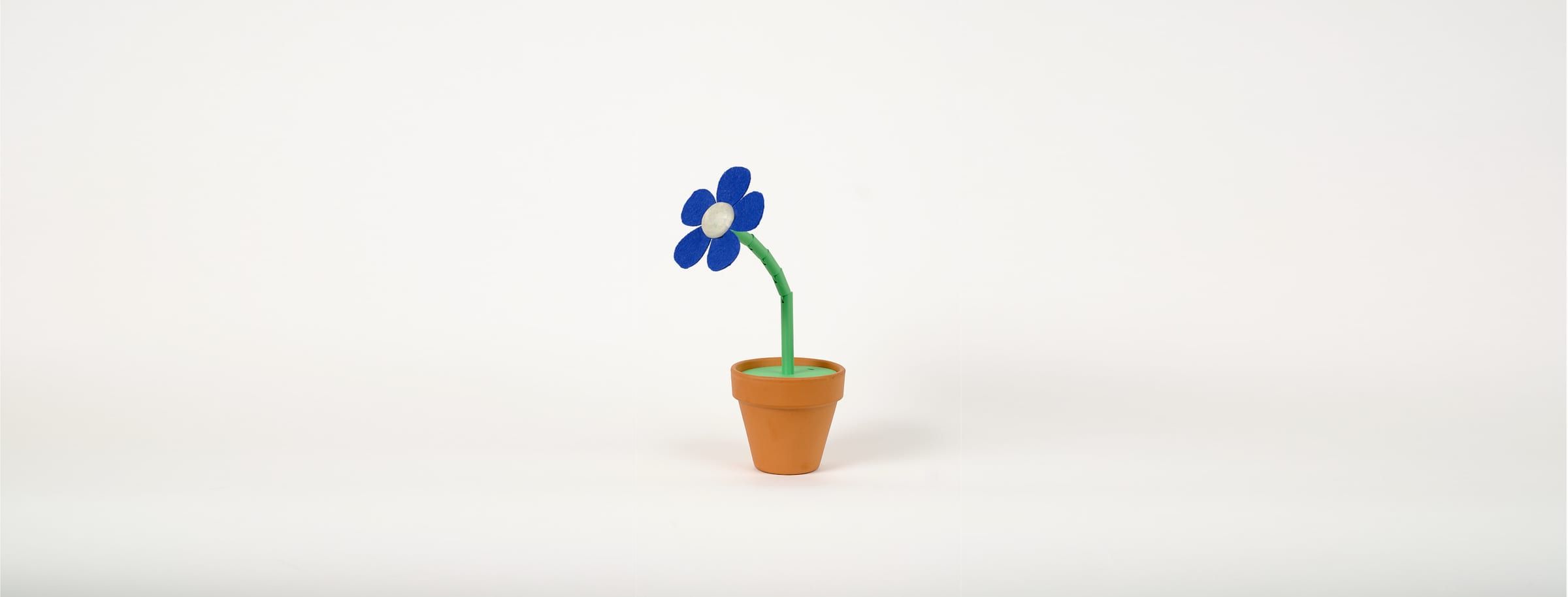 The finished DataBloom flower in a small terracotta pot — cobalt-blue felt petals, a pale 3D-printed center, a segmented green stem — on a white studio backdrop, surrounded by the 3D-printed parts and electronics it is built from.